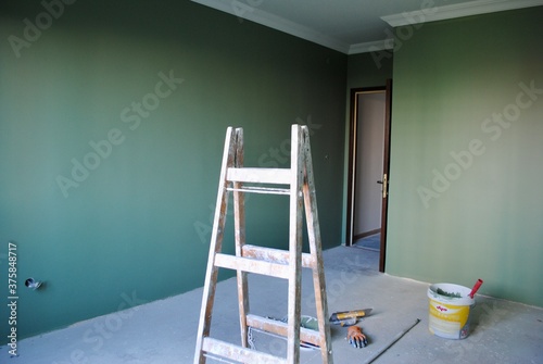 Room in renovation for relocation with newly dark green painted wall. Ladder, paint bucket, gloves and spatula on the floor. Renovation concept with copy space. 