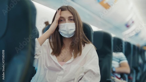 Sick young woman feeling unwell headache wearing face mask on plane transportation protect vacation coronavirus airplane ill holiday lady passenger close up slow motion