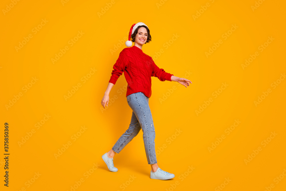 Full body profile photo of funny lady good mood walk friends place christmas party festive wear santa cap red knitted sweater jeans footwear isolated yellow color background Full body profile photo of funny lady good mood walk friends place christmas party festive wear santa cap red knitted sweater jeans footwear isolated yellow color background