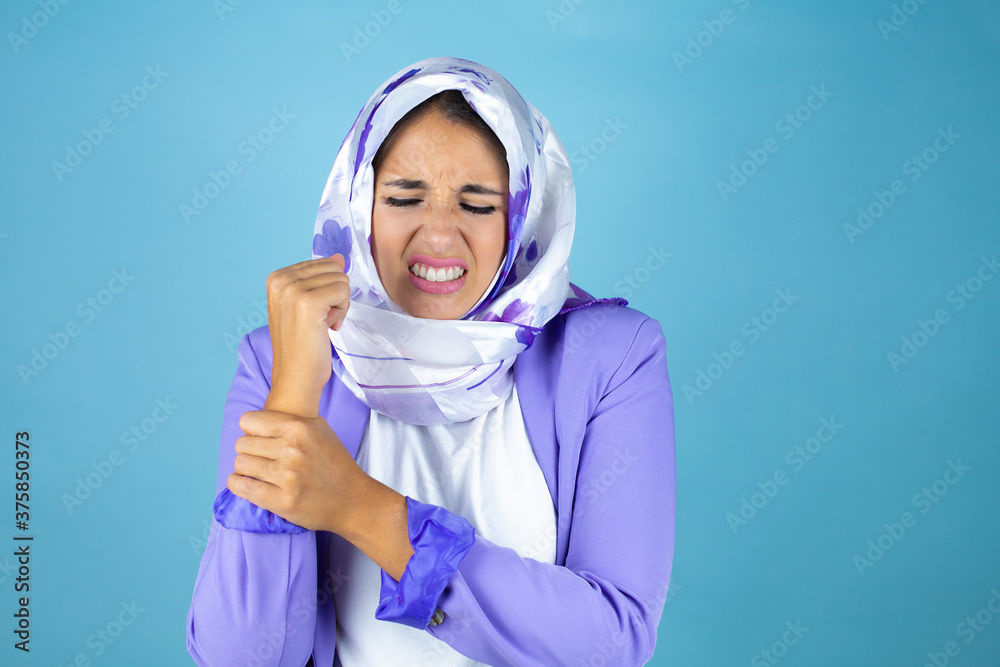 Young beautiful arab woman wearing islamic hijab over isolated blue background suffering pain on hands and fingers, arthritis inflammation