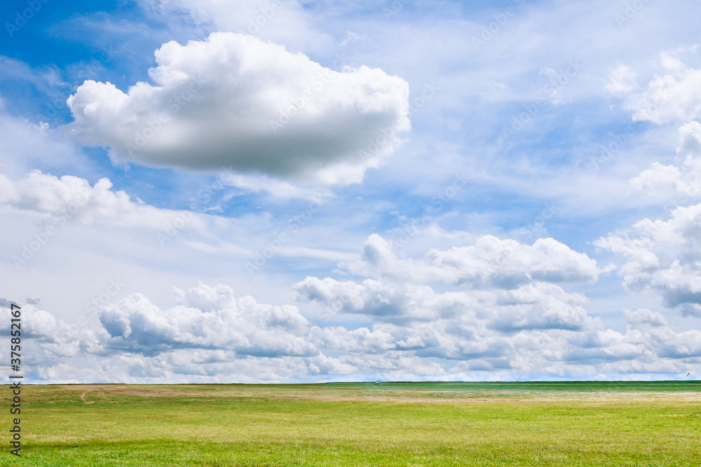 White clouds against a blue sky over a grassy field.