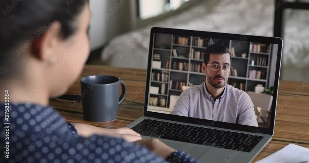 Job interview by videocall, hiring concept. Due corona virus or covid-19 businesspeople negotiate remotely use video conference app, laptop screen view over girl shoulder sit at desk talk by videocall
