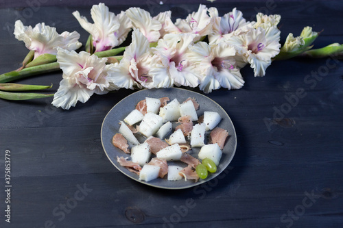 Gray Plate with melon and prosciutto on black wooden background and white gladiolus flowers decoration