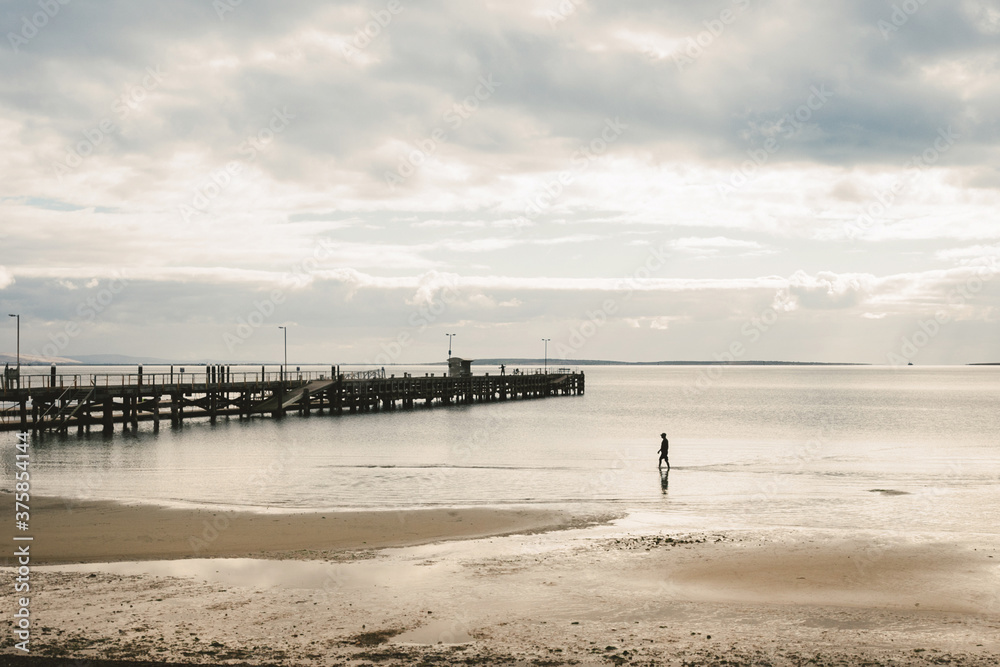 lone figure walking along the beach with a jetty or pier lone figure walking along the beach with a jetty or pier