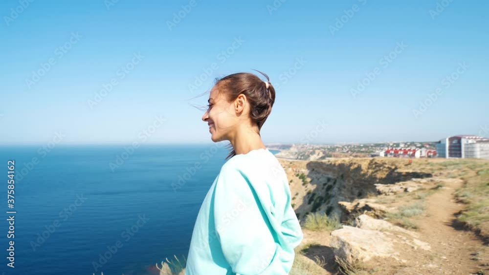 happy young woman traveler stands on background of amazing seashore with limewall cliffs and sky, hair blowing by wind. camera zooming in happy young woman traveler stands on background of amazing seashore with limewall cliffs and sky, hair blowing by wind. camera zooming in