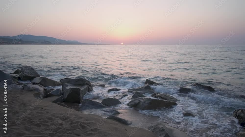 Ocean waves breaking in slow motion over rocks at the beach with beautiful sunrise in the background. Relaxing footage for meditation of calm sea at sunset. Summer holiday destination in Spain. Ocean waves breaking in slow motion over rocks at the beach with beautiful sunrise in the background. Relaxing footage for meditation of calm sea at sunset. Summer holiday destination in Spain.