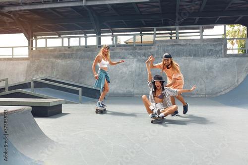 Skater Friends At Skatepark. Guy And Girls In Casual Outfit Riding On Skateboards. Summer Skateboarding With Modern Equipment As Part Of Active Lifestyle. Extreme Sport As Hobby.