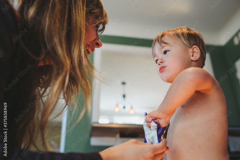 Young mother giving shirtless toddler boy a candy treat