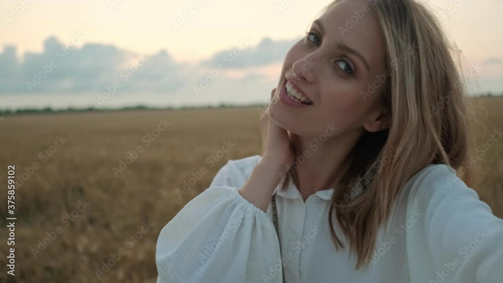 A beautiful young blonde woman is taking selfie-photo while walking on the field at summer A beautiful young blonde woman is taking selfie-photo while walking on the field at summer