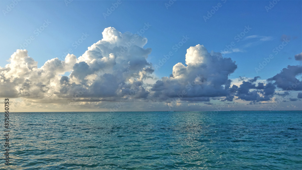 Obraz premium The white clouds over the Indian Ocean are illuminated by the sun. The aquamarine water is calm. Summer day, blue sky. Maldives. Male