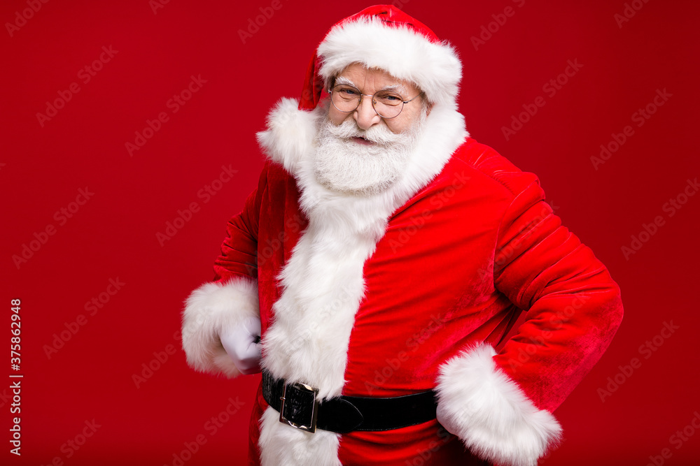 Photo of retired old man grey beard hands hips playful look self-assured ready long travel prepare sleigh wear santa costume belt coat spectacles headwear isolated red color background