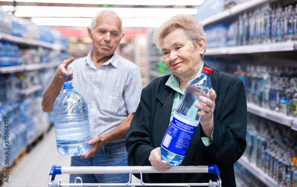 mature european spouses selects bottled water in the department of supermarket