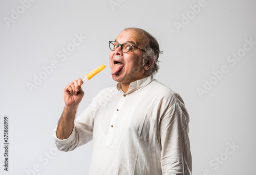 retired Indian old man eating ice cream, standing icolated against white background photo