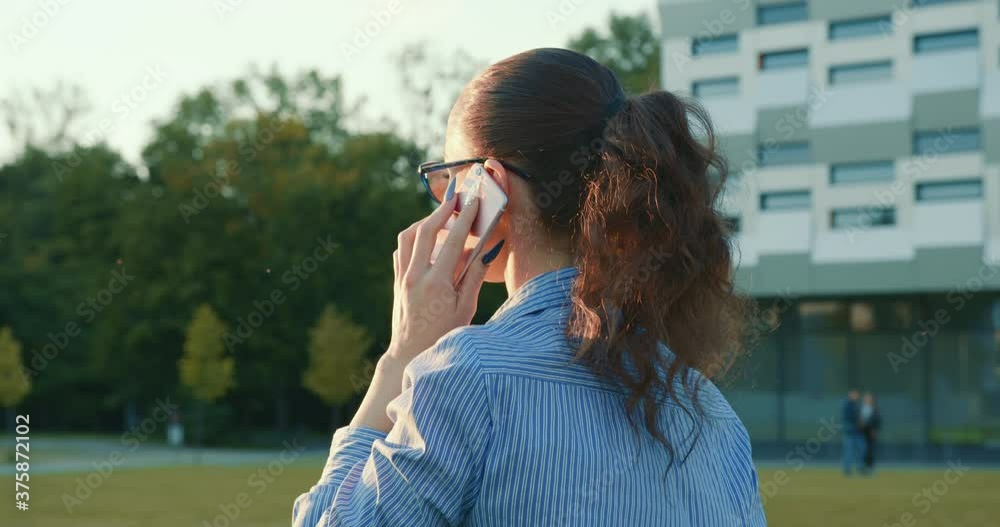 The businesswoman is walking and talking on the phone. Business center in the background. Close-up shooting. 4K The businesswoman is walking and talking on the phone. Business center in the background. Close-up shooting. 4K
