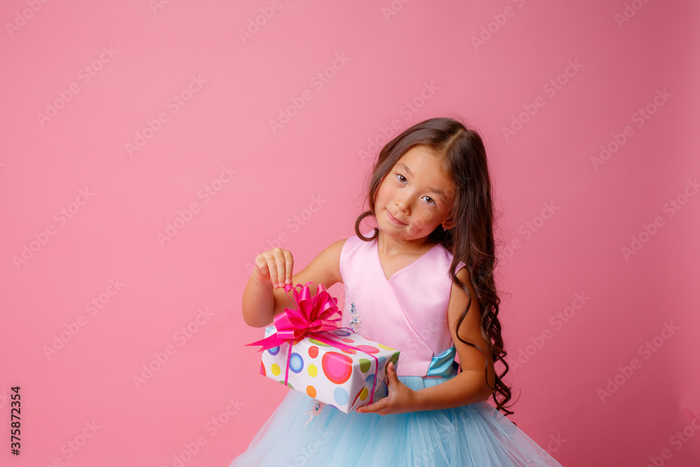a little girl of Asian appearance holds a gift in her hands celebrating her birthday on a pink background a little girl of Asian appearance holds a gift in her hands celebrating her birthday on a pink background