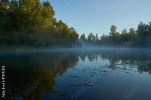 Autumn time. Dawn over the river in a misty  brooding haze. Beautiful view of the forest and river  covered with fog in the early morning. The sun s rays of light. September.