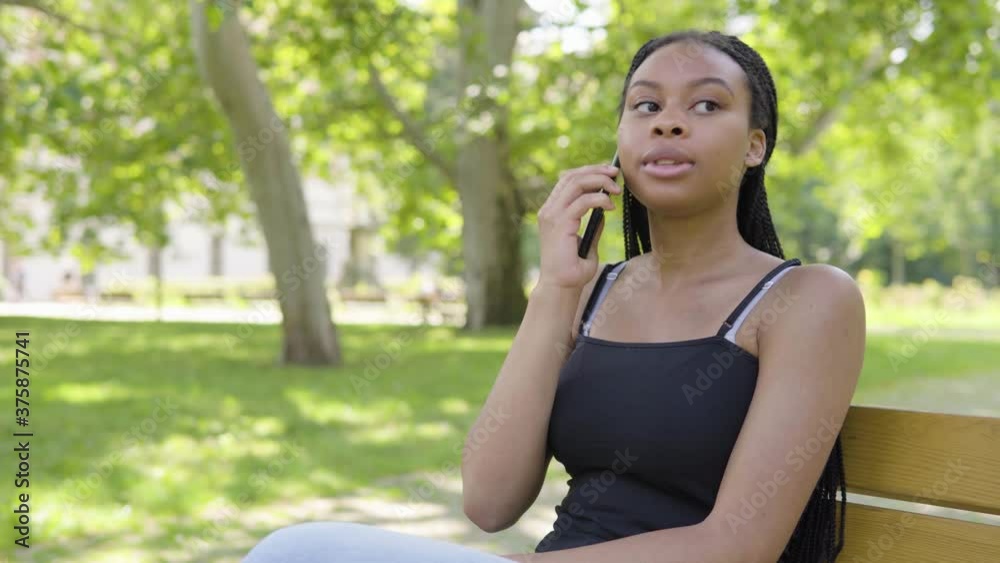 A young black woman talks on a smartphone and sits on a bench in a park on a sunny day A young black woman talks on a smartphone and sits on a bench in a park on a sunny day