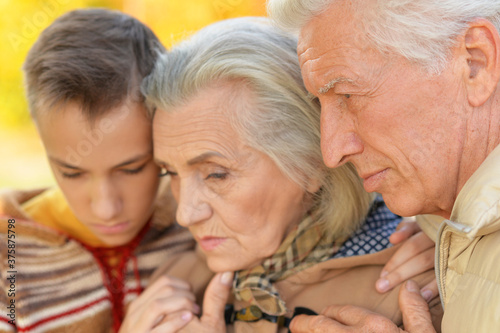 Close up portrait of sad grandfather, grandmother and grandson hugging