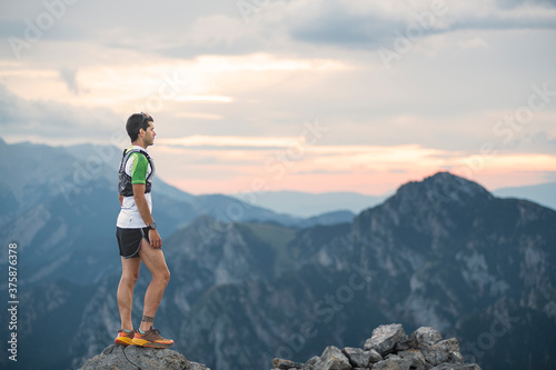 mountain running man standing on trail looking at sunset