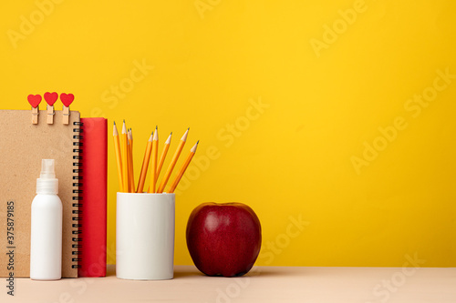 Cup of pencils and notepads on desk against yellow background