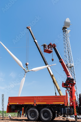 Construction of a wind power plant. Installers use a truck crane and aerial platform to raise the wind turbine rotor. Photo taken on a sunny summer day in Russia