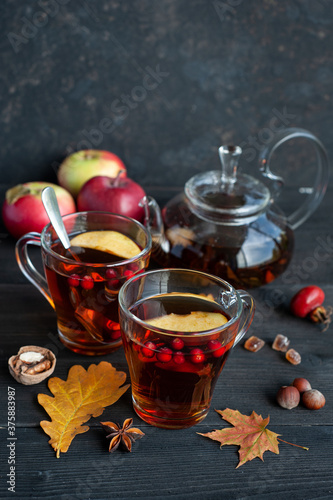 Two cups of autumn warming tea with berries and pieces of apples on a black wooden background. Hot berry tea.