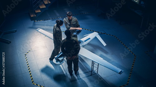 Army Aerospace Engineers Work On Unmanned Aerial Vehicle / Drone. Uniformed Aviation Experts Talk, Using Laptop. Industrial Facility with Surveillance, Warfare Tactics, Attack Machine. Elevated Shot