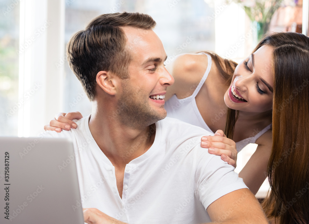 Fototapeta premium Happy excited smiling couple using laptop at home. Internet, shopping, online store or love concept - young man and woman looking at each other with computer.