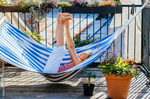 Foto Blond middle age woman stretching legs, relaxing in a hammock during summer holiday outdoor in terrace