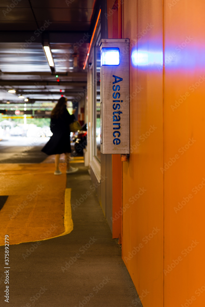 Garage parking with assistance box on orange wall and back view of young woman in black coat walking in soft focus background, Quebec City, Quebec, Canada Garage parking with assistance box on orange wall and back view of young woman in black coat walking in soft focus background, Quebec City, Quebec, Canada
