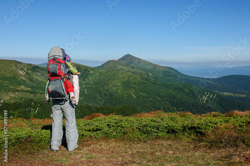 A sports mother with a child in a carrying backpack looks at Hoverla, the highest mountain of the Ukrainian Carpathians