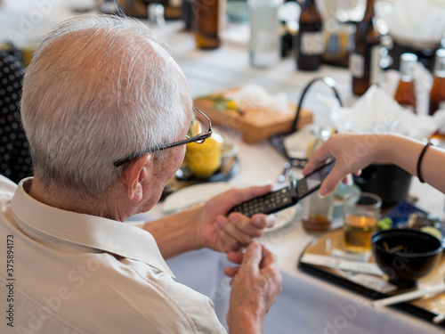 An elderly Asian man struggling to use an old fashioned flip phone