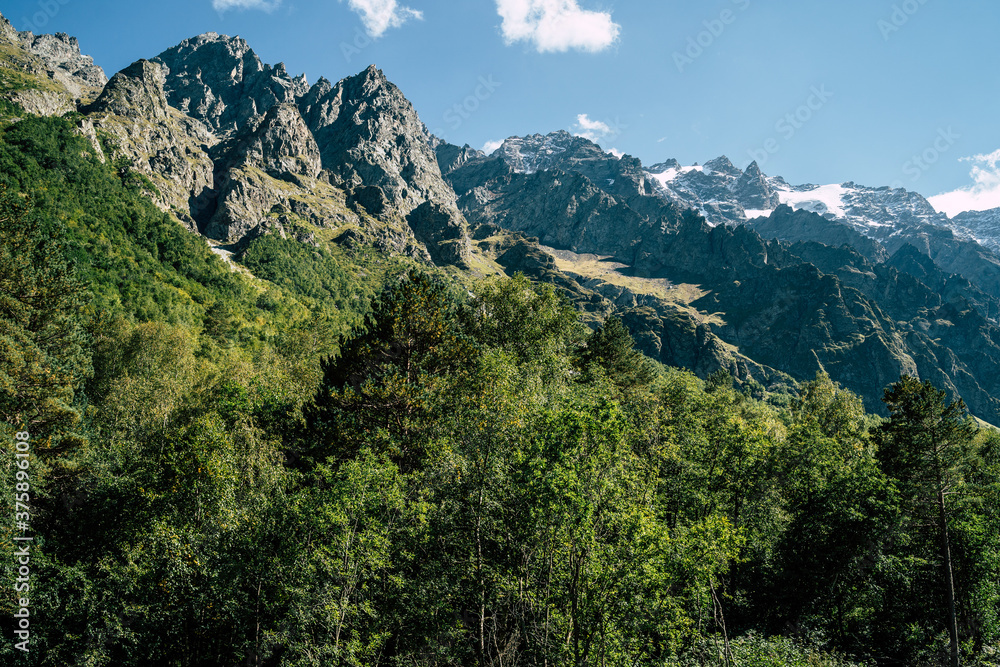 Mountain ridge covered with forest under blue sky. Picturesque scenery of mountain slopes and peaks covered with green lush foliage under blue sky in sunny summer day