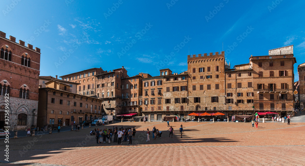 Gorgeous panorama image of various palazzi signorili at the famous Palazzo Pubblico (town hall) surrounding the Piazza del Campo on a sunny day with a blue sky in Siena, Tuscany, Italy.
