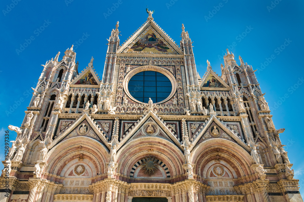 Perfect low-angle close-up shot of the west façade of the famous Duomo di Siena, a medieval cathedral in Siena, Italy. Built using polychrome marble, the work was overseen by Giovanni Pisano.