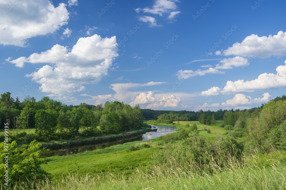Beautiful landscape with view from the hill to Salaca river in Latvia on summer sunny day running among green meadows and forest. Beautiful blue sky with white clouds over it.