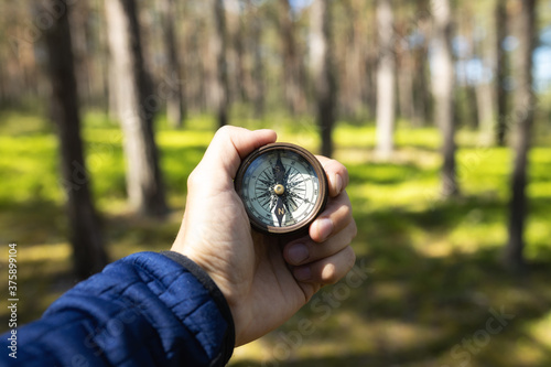 Closeup of hand holding old magnetic compass and showing directions in the forest.