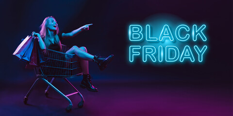Laughting, shopping. Portrait of young woman in neon on dark studio backgound. Human emotions, black friday, cyber monday, purchases, sales, finance concept. Copyspace. Seamless post for instagram.