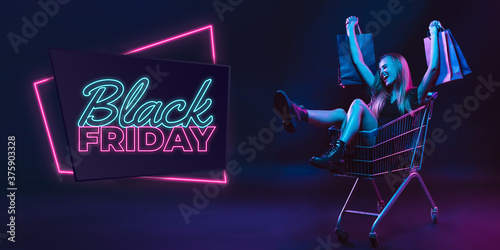 Laughting, shopping. Portrait of young woman in neon on dark studio backgound. Human emotions, black friday, cyber monday, purchases, sales, finance concept. Copyspace. Seamless post for instagram. photo