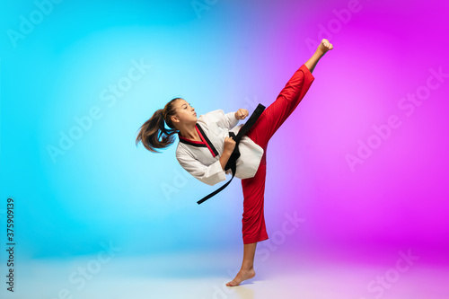 Fototapeta Naklejka Na Ścianę i Meble -  Powerful. Karate, taekwondo girl with black belt isolated on gradient background in neon light. Little caucasian model, sport kid training in motion and action. Sport, movement, childhood concept.