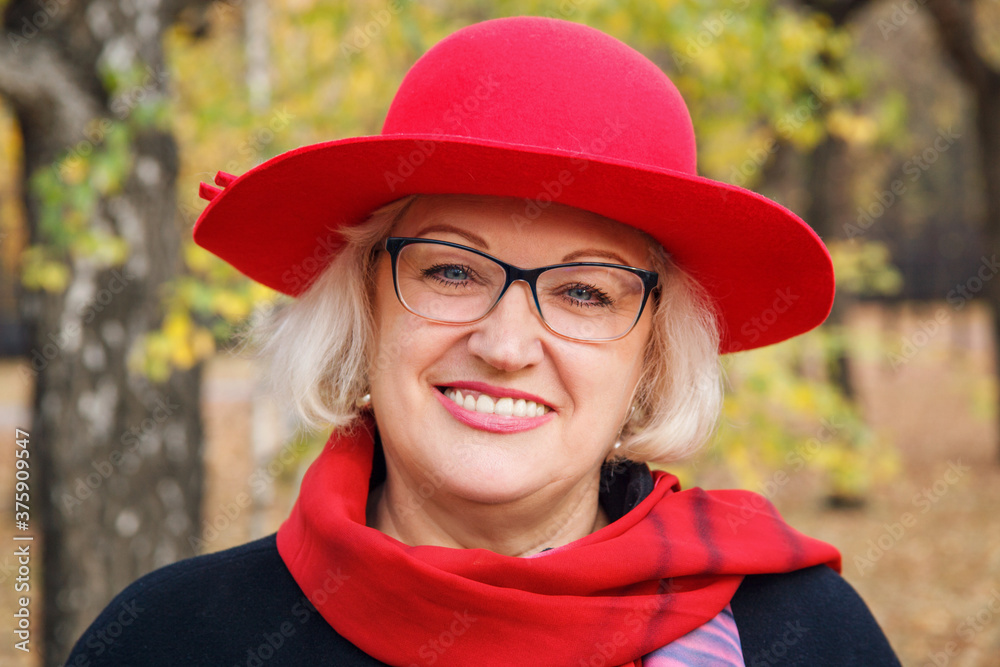 Portrait of mature woman in red hat and black coat in autumn park.