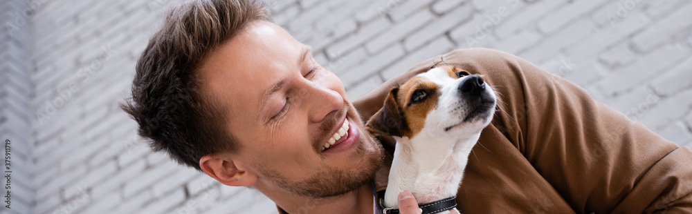 Fototapeta premium Horizontal image of man holding jack russell terrier near facade of building