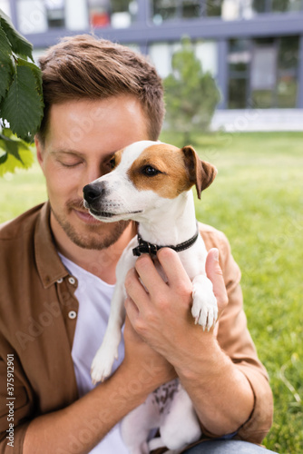 young man with closed eyes holding jack russell terrier dog with brown spots on head © LIGHTFIELD STUDIOS