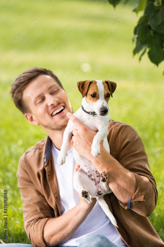 young man in brown shirt holding white jack russell terrier dog with spots on head young man in brown shirt holding white jack russell terrier dog with spots on head