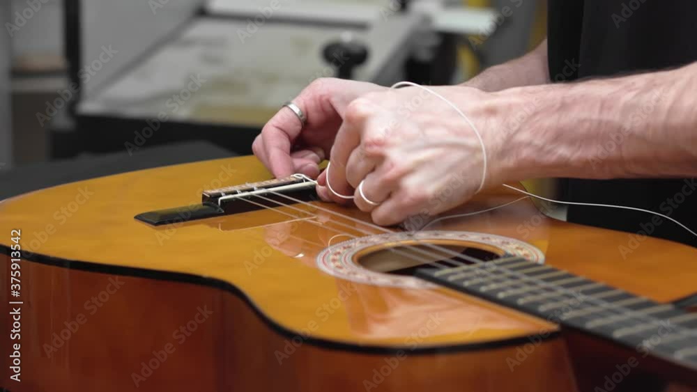 Caucasian luthier threads string on Spanish guitar. Detail hands shot Caucasian luthier threads string on Spanish guitar. Detail hands shot