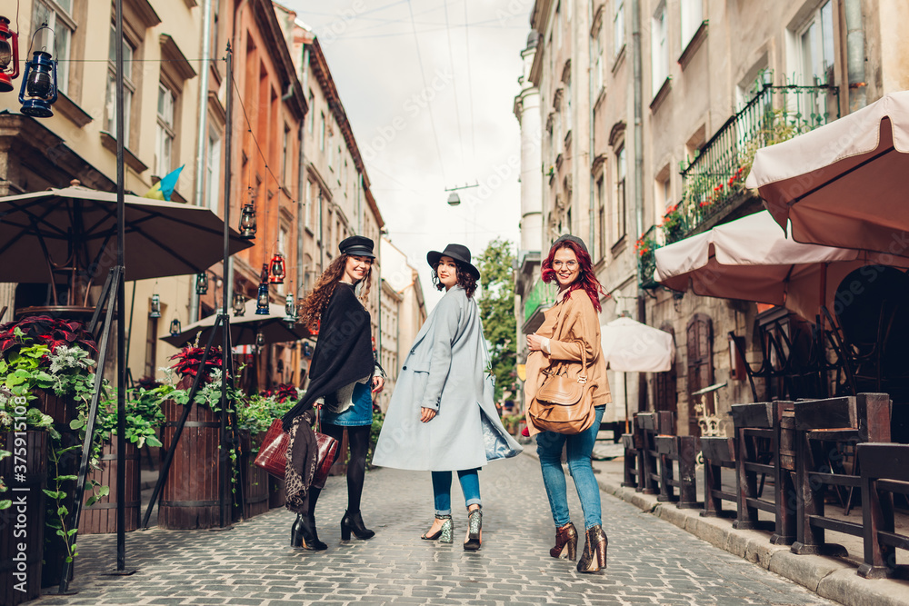 Stylish women walking on city street. Three girlfriends having fun in Lviv outdoors. Autumn fashion