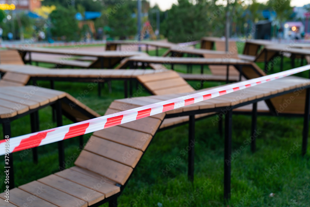 closed sports playground with wooden benches in a residential area, in a park, near the shopping center and deserted streets are sealed off with a barrier tape that prohibits passage during quarantine