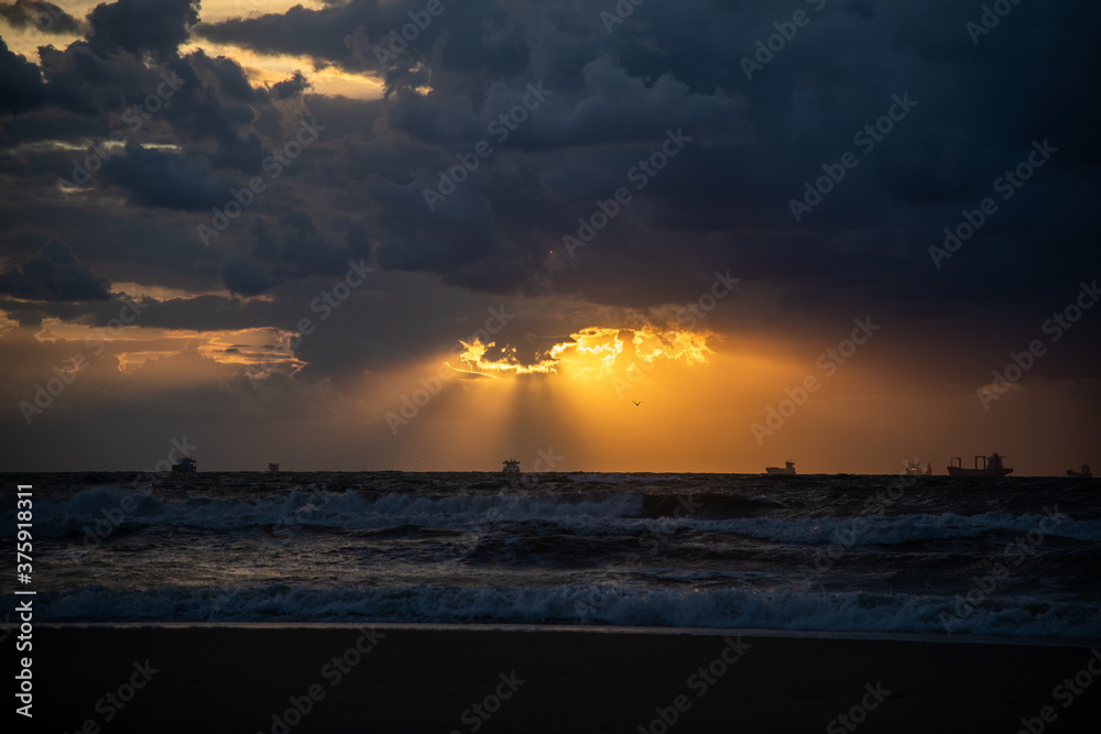 Beams of sunset light over ships and oil platform on the horizon at North Sea Beams of sunset light over ships and oil platform on the horizon at North Sea