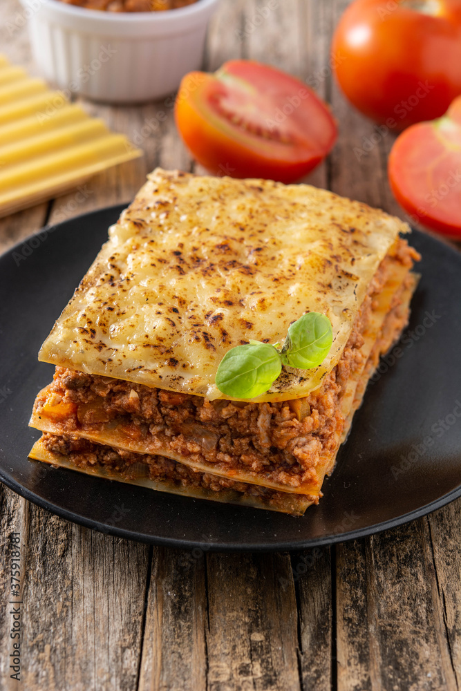 Piece of meat lasagna on black plate on rustic wooden table