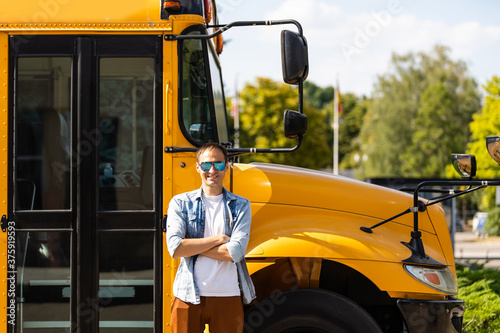 A happy male teacher near school bus